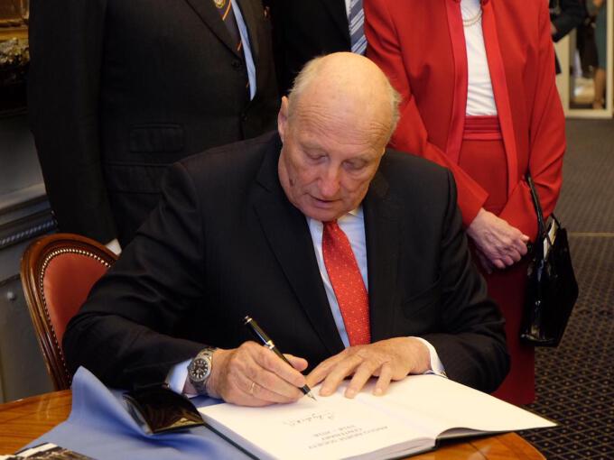 King Harald signs the guest book of the Anglo-Norse Society. Photo: The Royal Court, UK